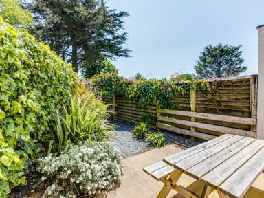 A garden area with a wooden picnic table plants and a wooden fence at Lowenna Manor 10 in Rock