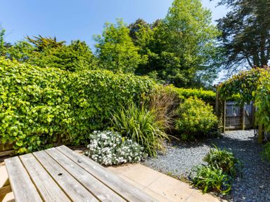 A garden area with a wooden picnic table gravel path plants and shrubs surrounded by a wooden fence at Lowenna Manor 10 Rock