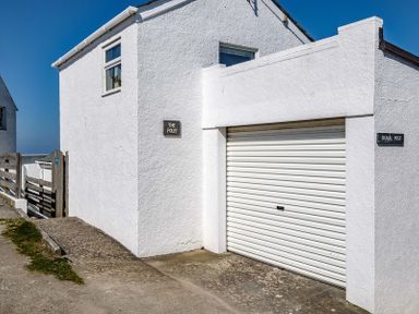 Exterior view of a white building with a garage door and signs that say The Folly and Signal Post at The Folly in Port Isaac
