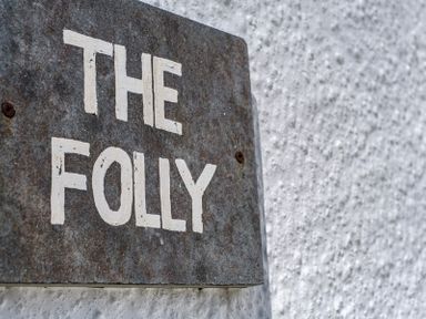 A metal sign with the words The Folly mounted on a white textured wall at The Folly in Port Isaac