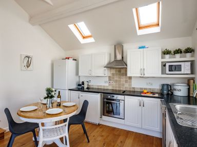 A kitchen with a round dining table set for four and white cabinets at The Folly in Port Isaac