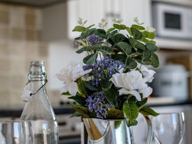 A close up of white and purple flowers in a metallic vase with glassware and kitchen items in the background at The Folly in Port Isaac
