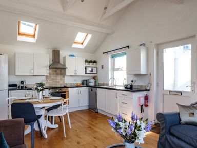 A kitchen with white cabinets and a dining table with chairs and a bouquet of flowers on the table at The Folly in Port Isaac