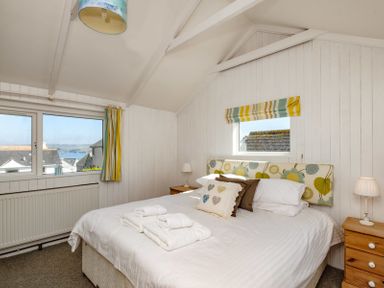 A bedroom with a bed set with white linens towels on the bed two wooden nightstands with lamps and windows with striped curtains at The Folly in Port Isaac
