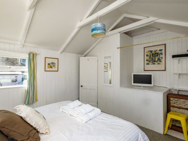 A bedroom with a bed a television on a cabinet and a window with striped curtains at The Folly in Port Isaac