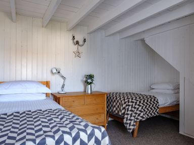 A bedroom with two single beds a wooden dresser with a lamp and flowers on top at The Folly in Port Isaac