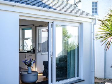 White house exterior with sliding glass door open showing a kitchen sink and flowers on a round table at The Folly in Port Isaac