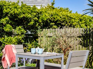 An outdoor patio table with two blue mugs a white teapot and a red cloth draped on a chair at The Folly in Port Isaac