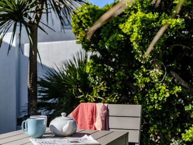 An outdoor table with a teapot two mugs and a newspaper with a chair and plants in the background at The Folly in Port Isaac