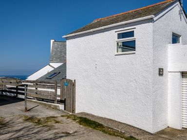 A white building with windows a wooden gate and a wooden fence under a blue sky at The Folly in Port Isaac