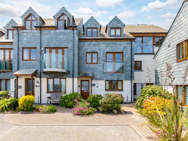 A row of houses with slate roofs and wooden windows with flower beds and benches outside at Rock Lobster in Port Isaac