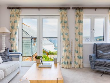 A living room with sofas a wooden coffee table and a view of buildings and sea through glass doors at Rock Lobster in Port Isaac