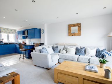 A living room with a gray sofa and blue kitchen cabinets at Rock Lobster in Port Isaac