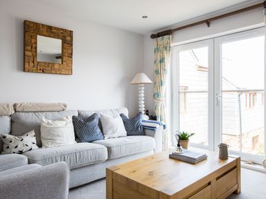A living room with a gray sofa, pillows, a wooden coffee table, a lamp, and large glass doors at Rock Lobster in Port Isaac