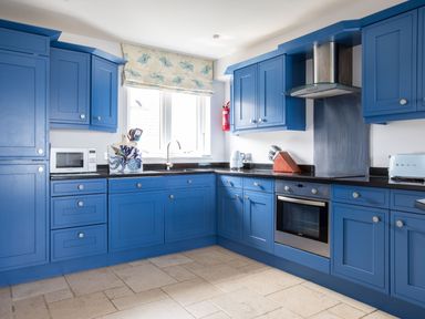 A kitchen with blue cabinets black countertops a microwave sink and oven at Rock Lobster in Port Isaac