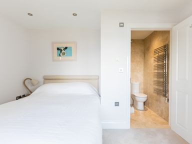 A bedroom with a bed and a lamp next to an open door leading to a tiled bathroom at Rock Lobster in Port Isaac