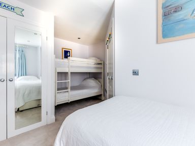 A bedroom with a double bed white bunk beds a wardrobe with mirrored doors and a painting on the wall at Rock Lobster in Port Isaac