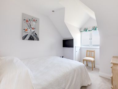 A bedroom with a bed white quilt a wooden chair a wall-mounted TV and a painting of ostriches at Rock Lobster in Port Isaac