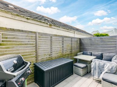 An outdoor patio area with a barbecue grill a black storage box a small table with cushioned seats and a corner sofa at Rock Lobster in Port Isaac