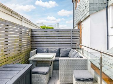 An outdoor patio with a wicker seating set including a corner sofa table and stools surrounded by wooden slat fencing at Rock Lobster in Port Isaac