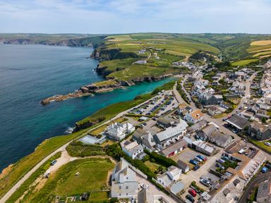 A coastal village with houses parking lots and green fields by the sea at Rock Lobster in Port Isaac
