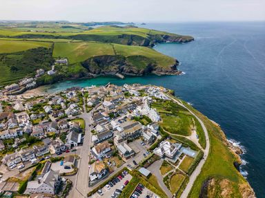 An aerial view of a coastal village with houses roads parked cars green fields and cliffs by the sea at Rock Lobster in Port Isaac