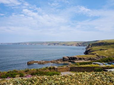 A coastal view with rocky cliffs a garden with flowers and parked cars at Rock Lobster in Port Isaac