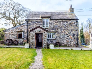 A stone cottage with a gravel path leading to an open wooden door and lawn at Dingles Cottage in Rock