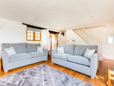 A living room with two grey sofas a grey patterned rug wooden floor and a staircase at Dingles Cottage in Rock