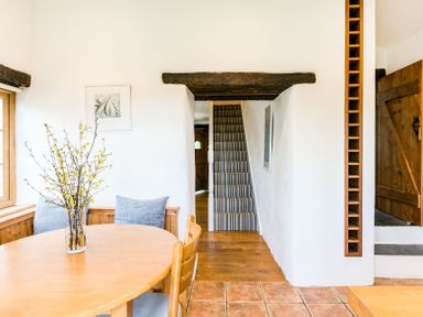 A dining area with a wooden table and chairs near a staircase with striped carpet at Dingles Cottage in Rock