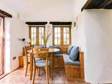A dining area with a wooden table chairs and a built-in bench with cushions at Dingles Cottage in Rock