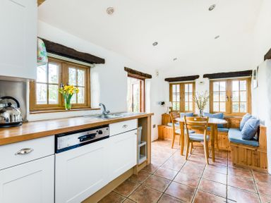 A kitchen with wooden countertops a sink a kettle and a dining area with chairs a round table and bench seating at Dingles Cottage in Rock