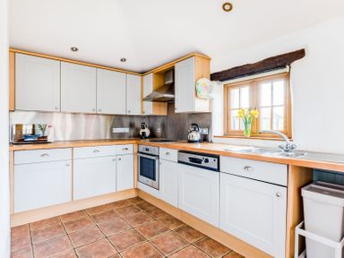 A kitchen with white cabinets a stove sink and a window with flowers on the windowsill at Dingles Cottage in Rock
