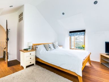 A bedroom with a wooden bed white bedding pillow with birds nightstand with lamp book window with blue shade at Dingles Cottage Rock