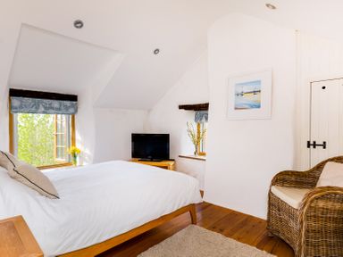 A bedroom with a bed a television a wicker chair and windows with floral curtains at Dingles Cottage in Rock