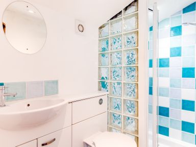A bathroom with a sink a round mirror a toilet a glass block partition and blue tiled shower at Dingles Cottage in Rock