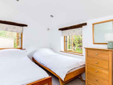 A bedroom with two single beds a wooden chest of drawers a mirror and two open windows at Dingles Cottage in Rock