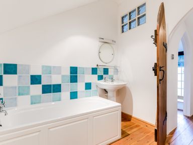 A bathroom with a white bathtub and sink with blue and turquoise tiled wall at Dingles Cottage in Rock