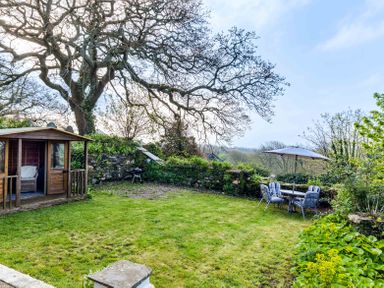 A garden with lawn chairs and a table under an umbrella near a wooden shed at Dingles Cottage in Rock