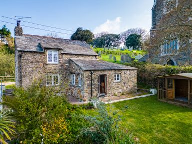 A stone cottage with tiled roof and garden next to a churchyard with gravestones at Dingles Cottage in Rock