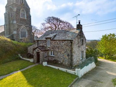 A stone cottage with a slate roof next to a large stone church with a tower and grass lawn at Dingles Cottage in Rock