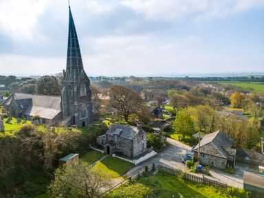 A stone church with a tall steeple next to stone houses and trees in a rural village