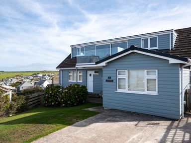 A blue two-story house with a glass balcony and driveway at Atlantis in Polzeath