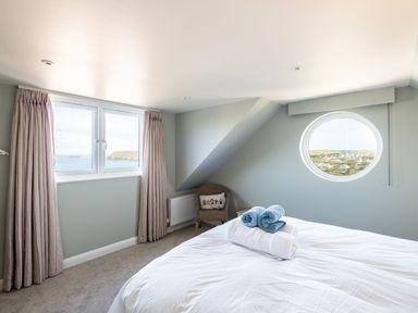 A bedroom with a bed and rolled towels near two windows with ocean and landscape views at Atlantis in Polzeath