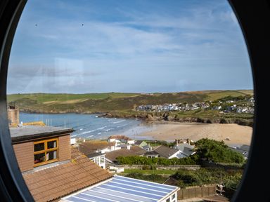 A coastal village with houses and a beach viewed through a round window at Atlantis in Polzeath