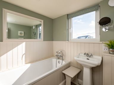A bathroom with a bathtub sink mirror window and small stool at Atlantis in Polzeath