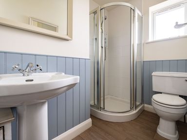 A bathroom with a pedestal sink a corner shower and a toilet with blue wainscoting on walls at Atlantis in Polzeath