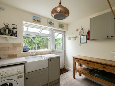 A utility room with a washing machine sink wooden table and a door with window at Atlantis in Polzeath