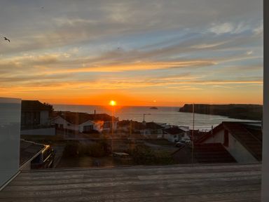 A sunset view over houses and the sea with birds flying above at Atlantis in Polzeath
