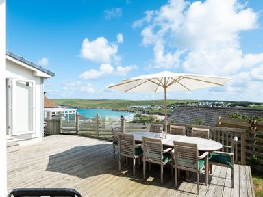 An outdoor wooden deck with a dining table, chairs, and a large umbrella overlooking a coastal landscape at Atlantis in Polzeath